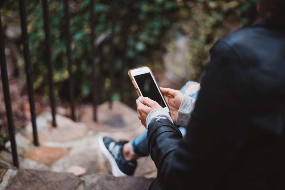Person sitting on steps holding a mobile phone, by Nadine Shaabana from Unsplash.com